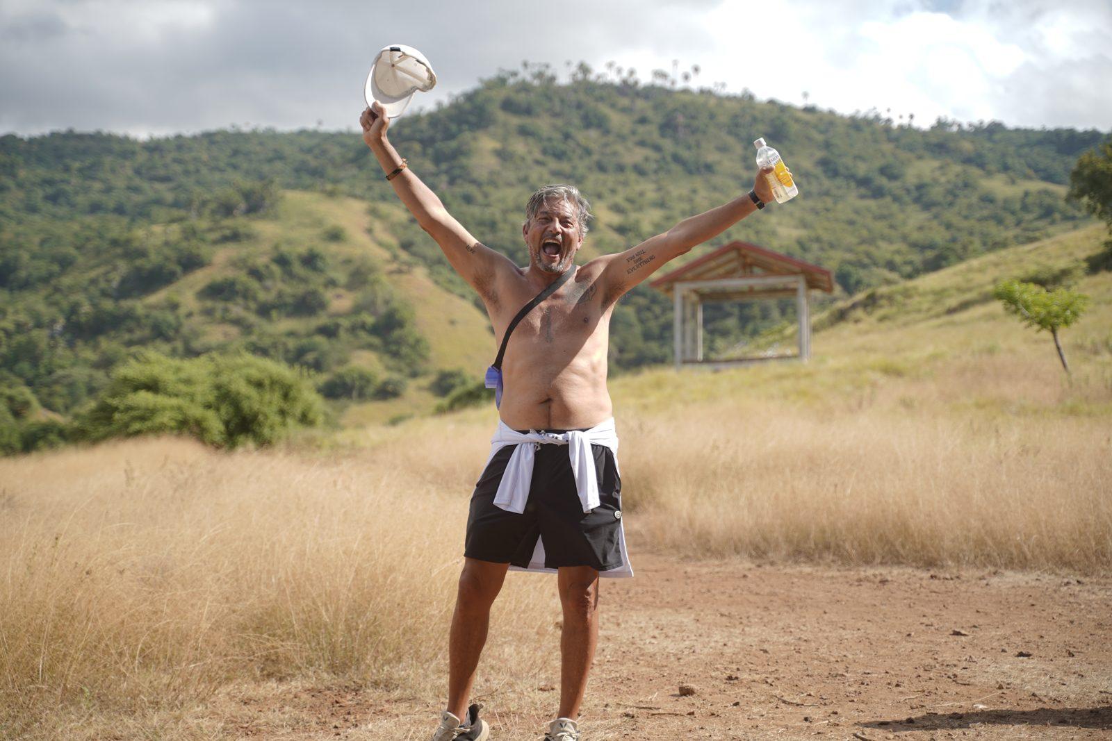 Komodo – Shirtless man cheering on savanna trail (Foto reale da un viaggio KEXI)